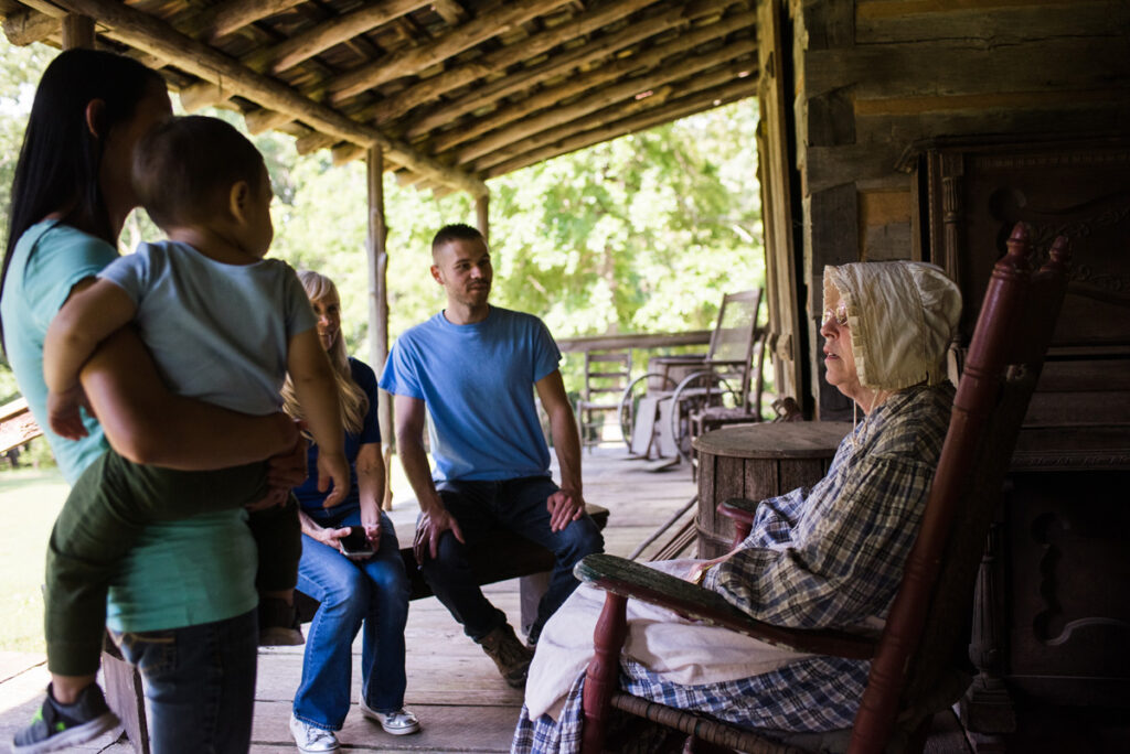 docent in rocking chair talks to family at log cabin