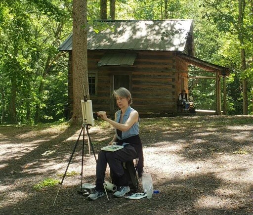 lady painting by a cabin